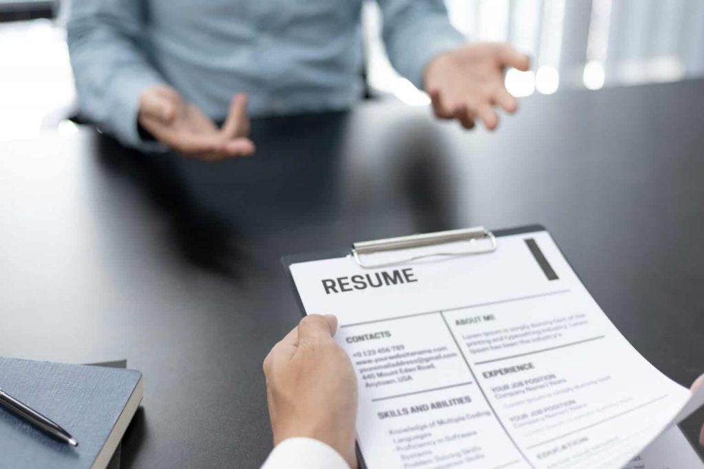 Point-of-view of an applicant holding their resume at a table with an interviewer